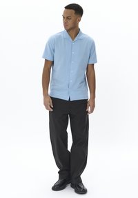 Camicia azzurro chiaro a maniche corte con colletto a scoperto, abbinata a pantaloni neri a gamba larga e scarpe nere. Tessuto piatto, design casual.