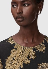 Must mustriga mustriga kuldse paisley ja lille tikandiga, ümmargune kaelus, näidates sujuvat tekstuuri ja elegantset disainitootet.