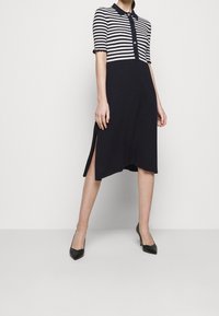 Abito navy con maniche corte a righe e colletto, caratterizzato da una placca con bottoni e fessure laterali, abbinato a tacchi neri a punta.