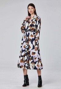 Robe à manches longues avec une jupe à volants, présentant un imprimé abstrait coloré dans des tons de marron, noir et lavande. Fini avec un col à boutons.