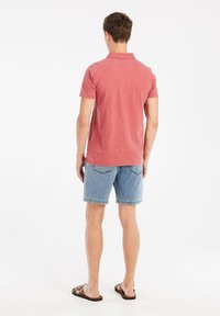 Rode katoenen polo met kraag, gecombineerd met blauwe denim shorts. Het shirt heeft korte mouwen en een relaxte pasvorm. Sandalen maken de look compleet.