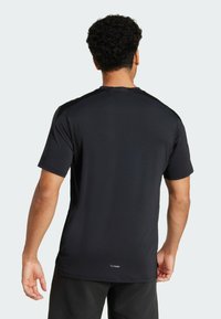 Camiseta deportiva negra de manga corta con cuello redondo y una textura ligera. Presenta un pequeño logotipo cerca del dobladillo y costuras suaves.
