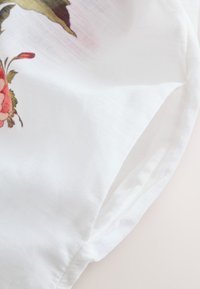 Material alb cu imprimeu floral roz și roșu și frunze verzi, prezentând o cusătură adunată și o textură moale.