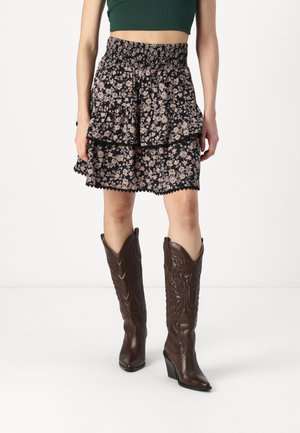 Falda mini negra con estampado floral, detalles de volantes en capas y cintura con fruncido, combinada con botas de cowboy marrones hasta la rodilla que presentan diseños intrincados.