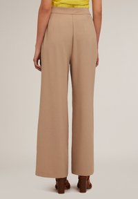 Beige wijde broek gemaakt van lichte stof, met een hoge taille en subtiele textuur, gecombineerd met bruine sandalen met hak.