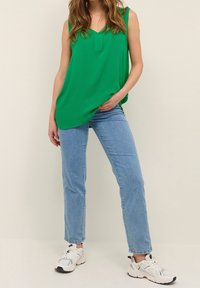 Top verde sin mangas con escote en V, combinado con jeans de talle alto de color azul claro. La modelo lleva zapatillas blancas con detalles en gris.