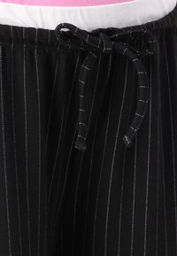 Pantalons de pyjama à rayures noires en tissu doux, avec une taille à cordon de serrage et des rayures blanches contrastantes, offrant une coupe décontractée.
