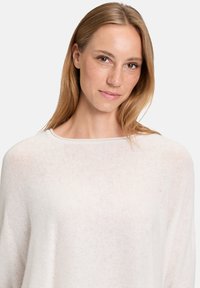 Pull en tricot léger, couleur crème, avec un large col, une coupe décontractée et une texture subtile. Idéal pour le superposition ou un look décontracté.
