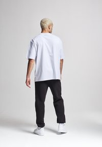 Weißes, übergroßes Baumwoll-T-Shirt mit Rundhalsausschnitt, kombiniert mit schwarzen, taillierten Hosen und weißen Sneakern, von hinten betrachtet.