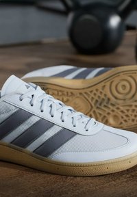 Witte sport schoenen hebben drie grijze strepen, een gestructureerde mesh bovenkant en een gumrubberen zool met een cirkelvormig loopvlak.