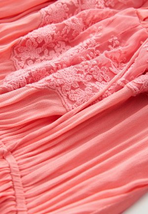 Tessuto di vestito color corallo con dettagli in pizzo intrecciato, caratterizzato da pieghe e una morbida texture uniforme. Design elegante con un effetto stratificato.