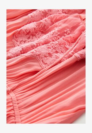 Țesătură de rochie corai roz, cu detalii intricate din dantelă, având pliseuri și o textură moale pe întreaga suprafață. Design elegant cu un aspect stratificat.