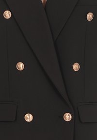 Blazer doppiopetto nero con bottoni color oro. Presenta rever a punta e tasche laterali, realizzato in tessuto liscio con un taglio su misura.
