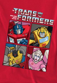 Red T-shirt featuring four cartoon Transformers: Optimus Prime (blue), Bumblebee (yellow), Megatron (black), and Arcee (pink), with graphic accents.