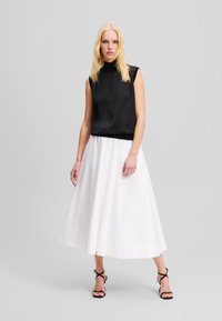 Melna bezpiedurkņu topa krekls, kas saskaņots ar baltu garu svārku ar pogām. Gluda auduma un eleganta dizaina apģērbs, papildināts ar melnām siksnu sandālēm.