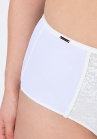 Culotte blanche taille haute avec un tissu lisse d'un côté et un panneau en dentelle de l'autre, dotée d'une mince bande et d'un accent logo subtil.