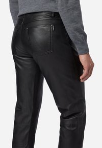 Zwarte leren broek met een gladde textuur, voorzien van twee achterzakken en subtiele stiksels langs de zijkanten en zakken.