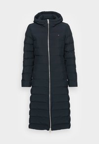Marineblå lang pufferjakke med hætte, med en frontlynlås og kviltet design. Stofoverfladen ser glat ud med en let glans.