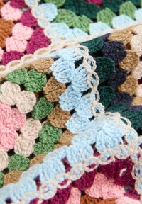 Carrés granny multicolores crochetés reliés par des boucles beiges, avec des fils verts, bleus, roses, marron, turquoise et bordeaux dans un motif texturé.