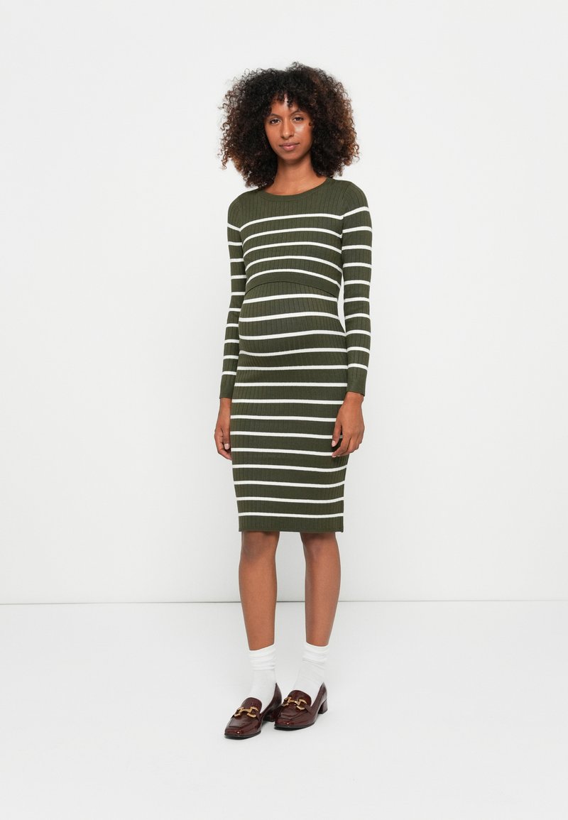 Abito a maglia verde oliva con righe orizzontali bianche, maniche lunghe, silhouette aderente, lunghezza al ginocchio, abbinato a mocassini marroni e calze bianche.