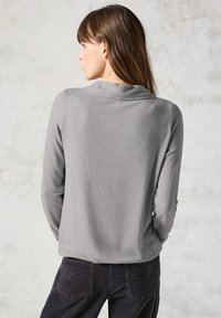 Grå långärmad topp med en subtil textur och avslappnad krage, matchad med mörka kordbyxor. Enkelt och funktionellt design.