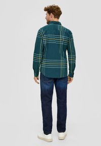 Groene geruite blouse met gele strepen, knoopsluiting, lange mouwen en een detail op de rug. Gecombineerd met donkerblauwe denim jeans en witte sneakers.