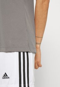 Šedé atletické tričko s krátkymi rukávmi, vyrobené z hladkej textílie, skombinované s bielymi šortkami s čiernymi pruhmi a logom adidas.