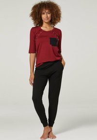 Maroon shirt with black pocket and snap details, paired with black tapered pants. Soft fabric, three-quarter sleeves, and relaxed fit.