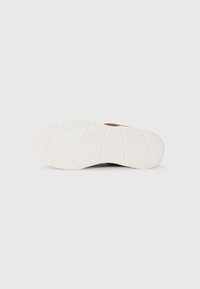 Brown shoe sole with textured white rubber, featuring a geometric pattern and pronounced tread for grip. Clean, minimal design without embellishments.