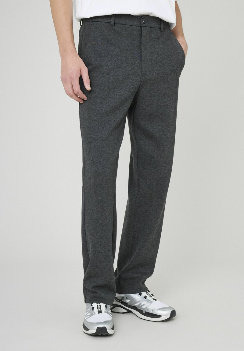 Pantalon gris en tissu texturé avec une coupe droite, doté de poches latérales et d'une taille à boutons. Porté avec des chaussures de sport argentées.