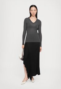 Gray ribbed long-sleeve top paired with a black, asymmetrical midi skirt. White pointed-toe flats and a small structured handbag complete the look.