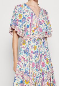 Ein Blumenkleid mit hellen Farben, V-Ausschnitt, kurzen Flatterärmeln, taillierter Silhouette und komplizierten Mustern von Vögeln und Blumen.