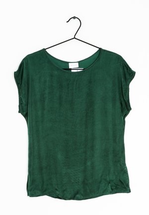 Blouse courte à manches courtes de couleur vert foncé avec col rond, suspendue à un cintre en fil noir sur fond blanc.