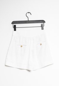 Shorts blancs en tissu lisse, avec une taille froncée, deux poches avant ornées de boutons dorés, et une coupe décontractée.