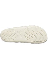 Suola di gomma bianca con un motivo di presa testurizzato, caratterizzata da scanalature e creste curve per una maggiore trazione. Include il marchio sulla parte intermedia.