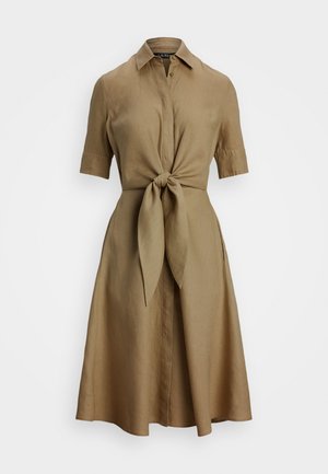 Beige linnekjol med knäppning fram, korta ärmar och knytning i midjan. Utrullad kjol och slät yta. Inga mönster eller hårdvara synliga.