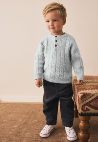 Pull bleu clair en maille avec motif torsadé, orné de trois boutons marron. Pantalon en velours côtelé noir et baskets blanches complètent la tenue.