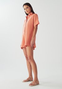 Persikofärgad skjortklänning med korta ärmar, krage, knäppning fram, en bröstficka och lös passform, kombinerad med remsandaler.