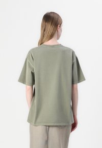 Olive green oversized t-shirt with short sleeves, round neckline, and stitching details, made from soft cotton fabric. Back view shown.