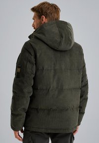 Donkergroene pufferjack met een gestructureerde corduroy afwerking. Kenmerken zijn een grote capuchon en zichtbare stiksels met een merkembleem op de mouw.