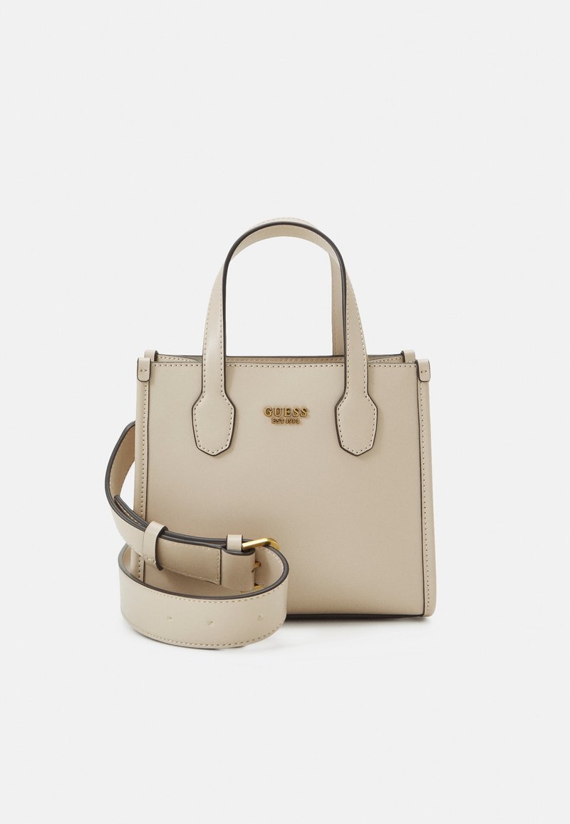 Sac à main structuré beige avec doubles poignées, bandoulière réglable et logo doré « GUESS » à l’avant, sur fond blanc.