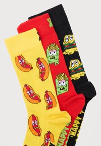 Τρία ζευγάρια πολύχρωμες κάλτσες με κινούμενους χαρακτήρες φαγητού: κίτρινα χοτ ντογκ, κόκκινες πατάτες τηγανιτές και μαύρα cheeseburgers με εκφραστικά μάτια.