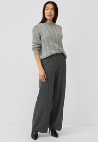Grau gestrickter Pullover mit Zopfmuster und hohem Kragen, kombiniert mit weit geschnittenen dunkelgrauen Hosen. Schwarze Pumps runden das Outfit ab. Schlichtes, strukturiertes Design.