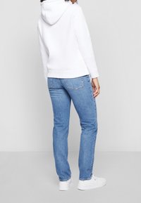 Hvid hættetrøje kombineret med lyseblå slim jeans og hvide sneakers, der viser en afslappet pasform og enkel design.