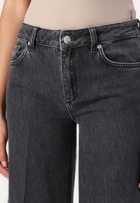 Sorte høye midjejeans laget av denim, med frontlommer, knappe- og glidelås-lukking, samt sømdetaljer langs sømmene.