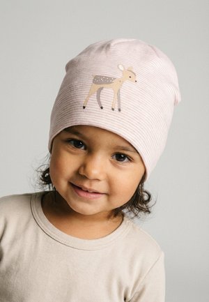 Toddler with dark hair wearing a light pink striped beanie featuring a small deer illustration, smiling softly against a plain background.