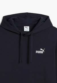 Námořnická modrá mikina s kapucí s fleecovou podšívkou, na levé straně hrudi s bílým vyšitým logem "PUMA". Obsahuje šňůrky.