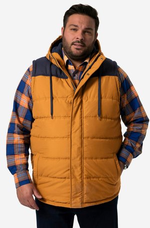 Geel-bruine puffer vest met marineblauwe accenten, voorzien van een capuchon, voorzakken en een gewatteerde textuur. Draagt over een geruite overhemd met knopen.