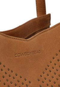 Borsa a mano in pelle marrone con design perforato e logo impresso. Presenta una texture morbida, parte superiore arrotondata e una tracolla resistente.