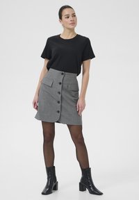 Jupe gris à rayures avec fermeture à boutons sur le devant, deux poches plaquées et une coupe ajustée. Associée à un t-shirt noir à manches courtes et des bottines noires.